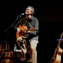 photo of Dennis Warner singing and playing guitar in concert