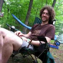 photo of Drew Grunseth sitting in a chair in a campsite in the woods